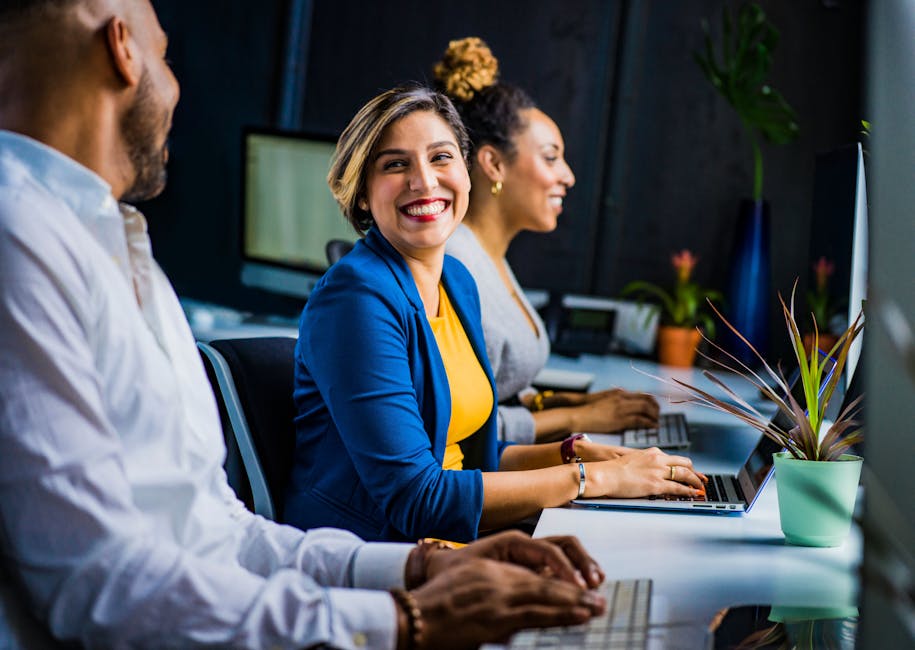Three diverse professionals working and smiling at office desks, fostering teamwork and collaboration