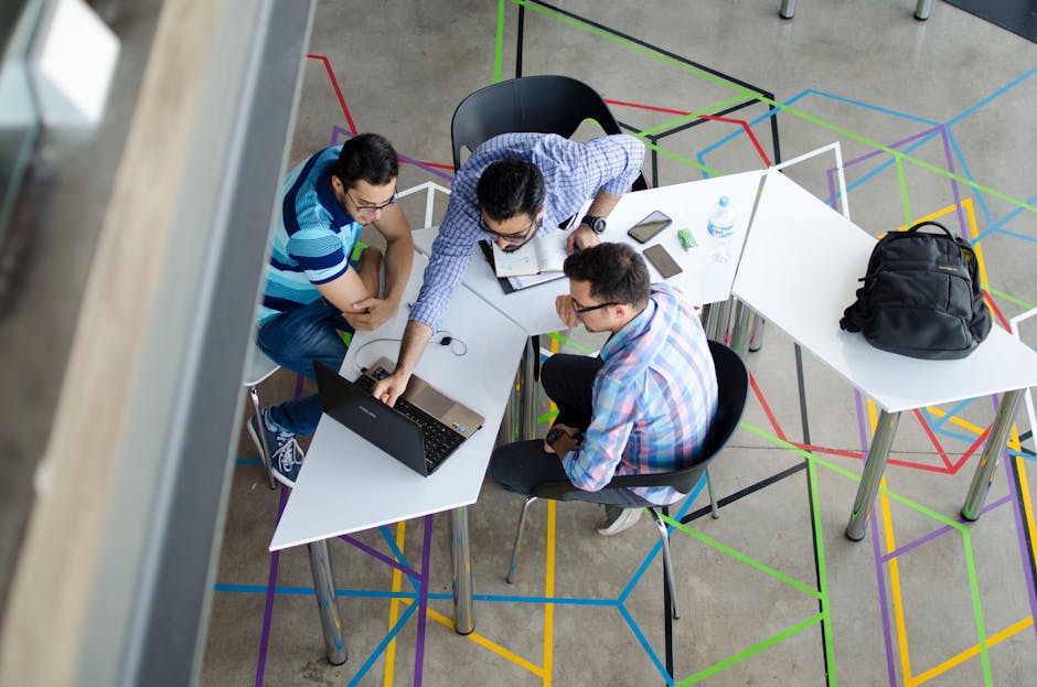 Three men collaborating over a laptop in a modern, geometric-themed office space