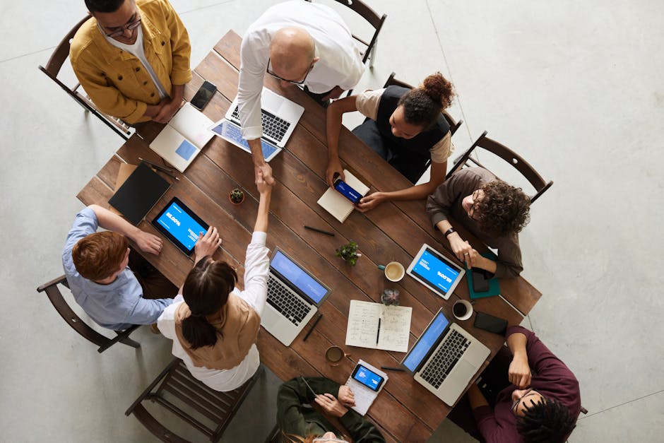 Top view of a diverse team collaborating in an office setting with laptops and tablets, promoting cooperation