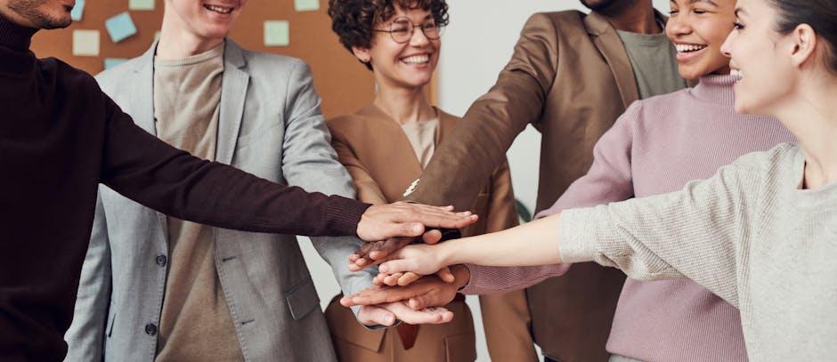 A group of happy, diverse colleagues celebrating teamwork and cooperation with a group high five indoors